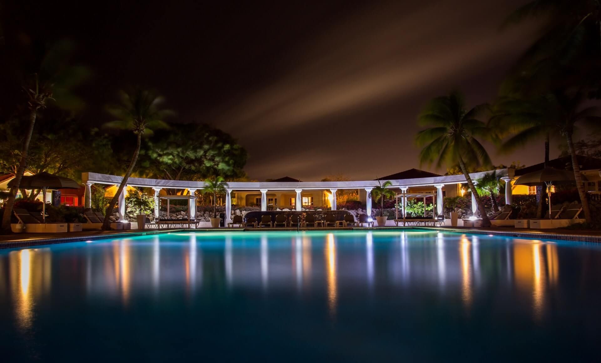 Hotel pool lit at night, palm trees reflected in still water